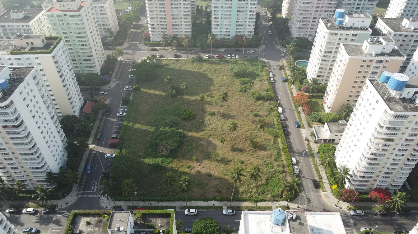 An aerial view showcases a large undeveloped land parcel located in a tropical city, surrounded by modern residential condominiums. This site, potentially a future government land sales site, hints at upcoming property investment opportunities in the area, which may influence land prices and launch prices per square foot.